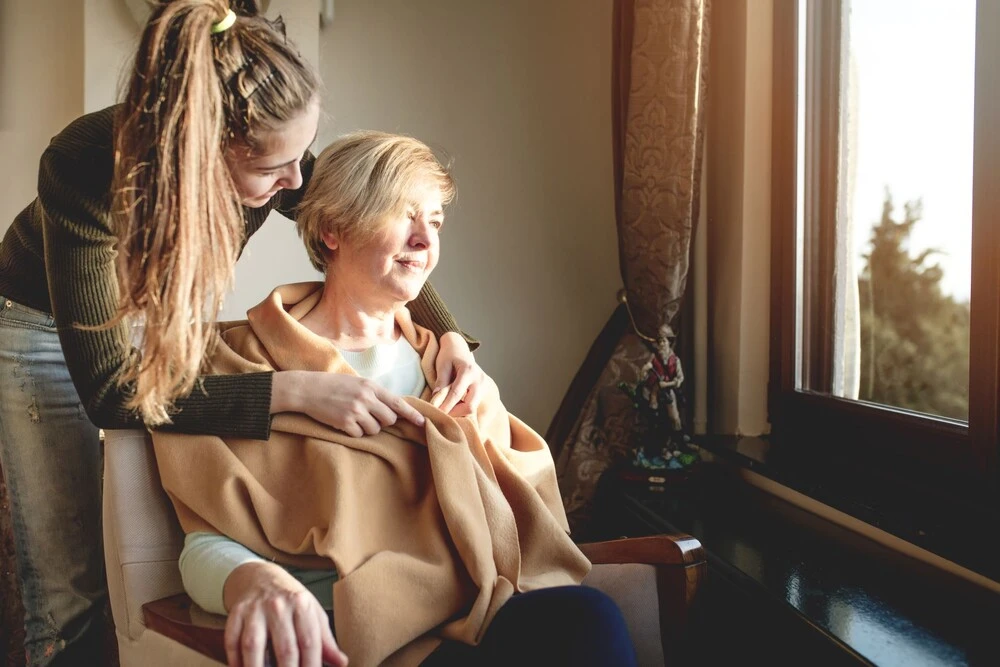 Younger women draping a blanket on an older woman sitting in a chair